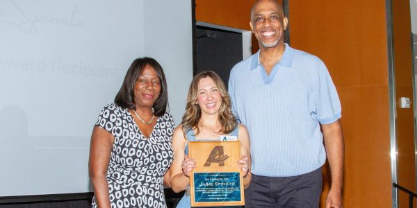 Three people smiling, one holding an award plaque.