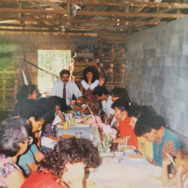 Reunión familiar en un comedor sencillo con comida y flores.