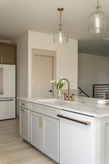 Modern kitchen island with white countertop and brass fixtures.
