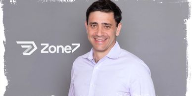 Smiling man in white shirt with Zone7 logo on gray background.