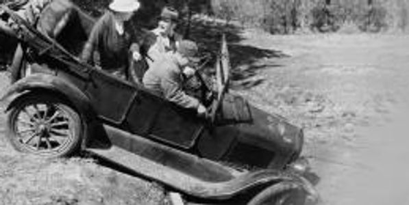 Old car stuck in a ditch with people trying to get it out.
