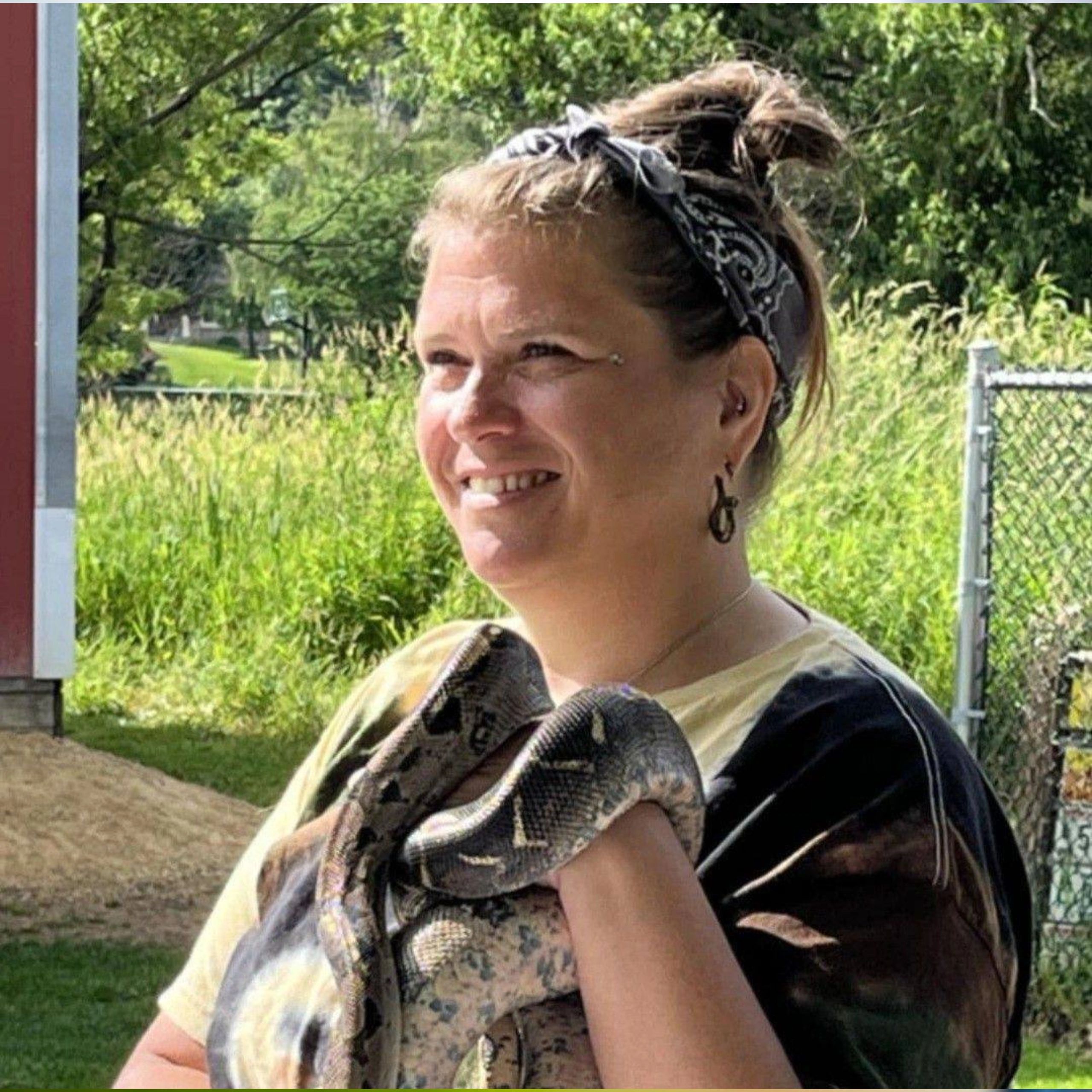 A smiling woman holding a large snake outdoors on a sunny day.