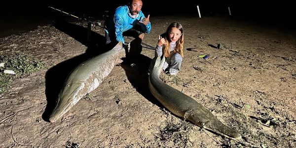 Two people proudly display two large fish they caught at night.