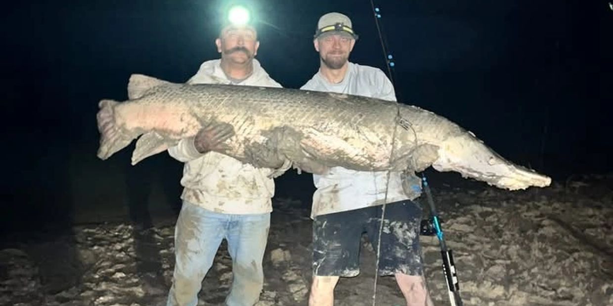 Two men holding a large fish at night, muddy and proud.