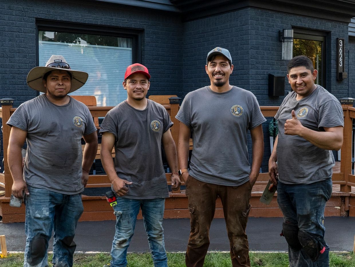 Four construction workers posing outdoors in front of a house.