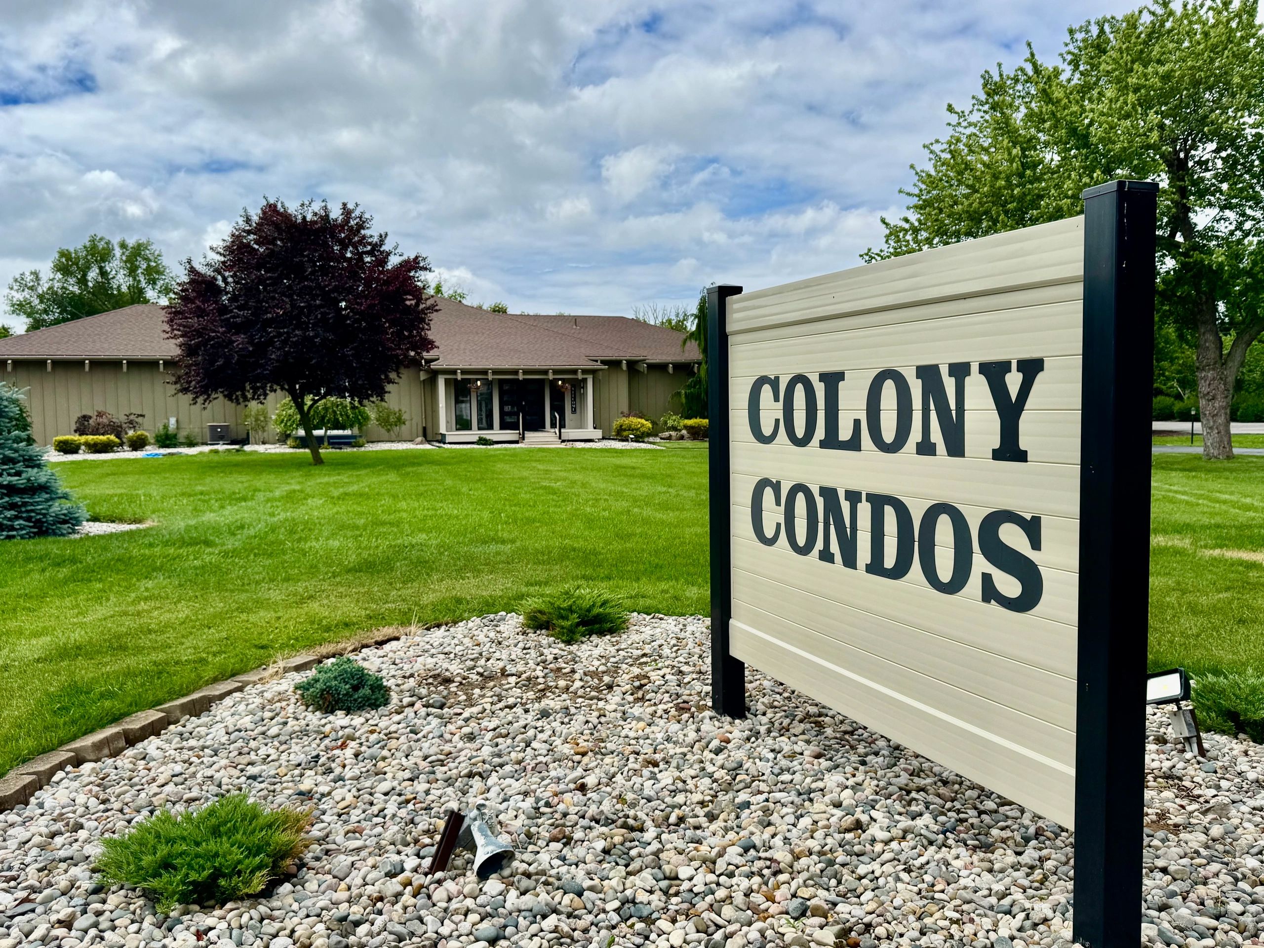 Sign for Colony Condos with building and lawn.