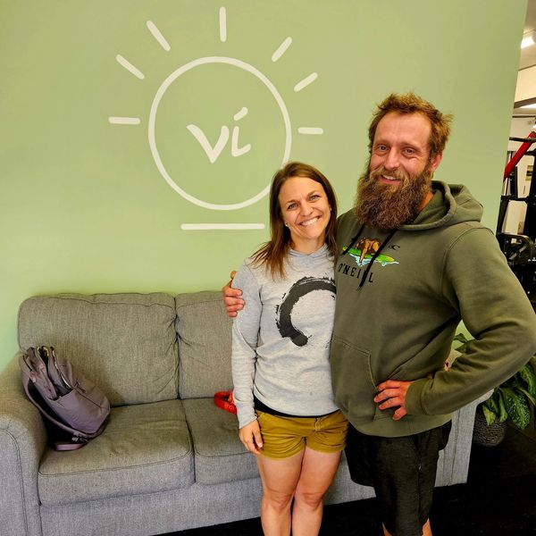 A smiling couple posing in front of a green wall with a lightbulb logo.