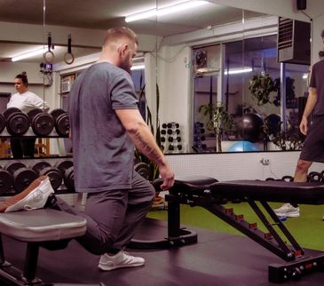 Man stretching in a gym near a bench and dumbbells.