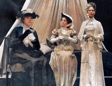 Three women in vintage dresses and hats posed indoors.