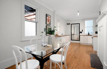 Bright dining area with glass table and white chairs on wooden floor.