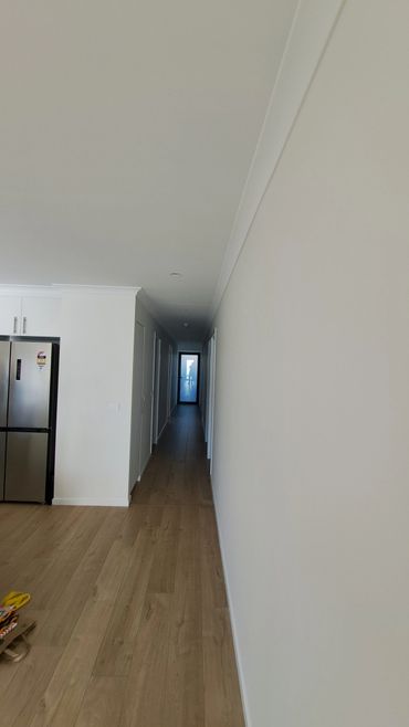 Long, narrow hallway with wooden floor and white walls leading to a glass door.