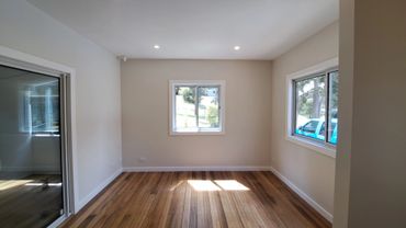 Empty room with wooden flooring and white walls illuminated by natural light.