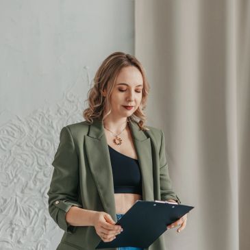 Kobieta w zielonej marynarce trzymająca teczkę i patrząca na nią.