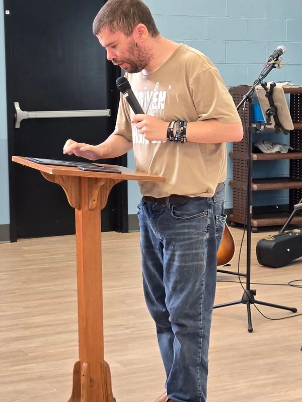 Man speaking with a microphone at a wooden podium.