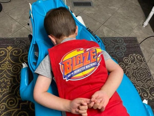 Child lying face down on a blue chair wearing a Blaze shirt.