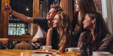 three women and a man clicking selfie together 