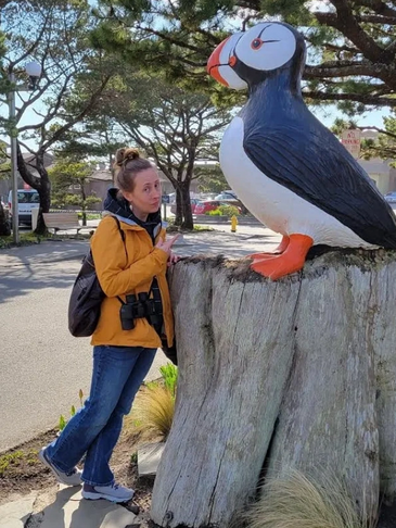 Natalie stands in front of an Atlantic Puffin sculpture while pointing with a silly face
