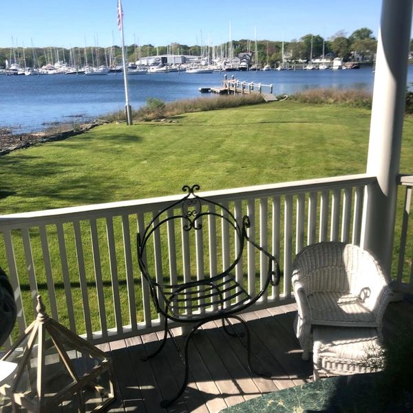 Porch with two chairs overlooking a grassy lawn and marina with boats.