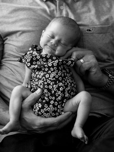 Sweet photograph of newborn baby blissfully sleeping in father's arms
