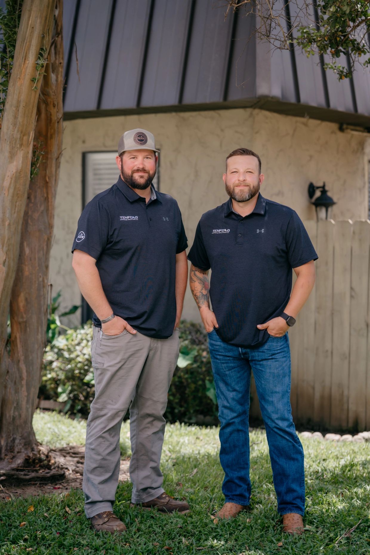 Two men standing outside wearing matching black Tenfold polo shirts.