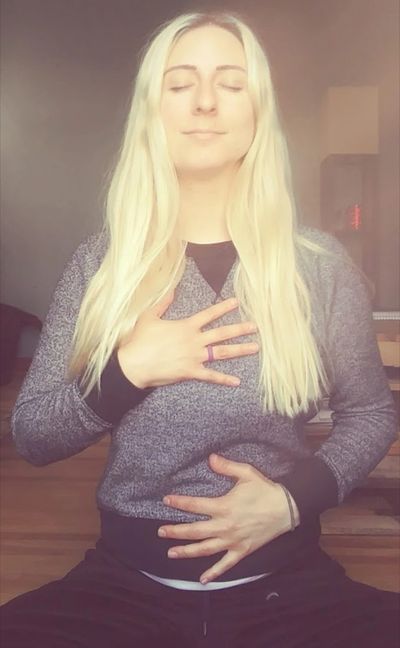 Woman meditating with eyes closed and hands on chest and stomach.