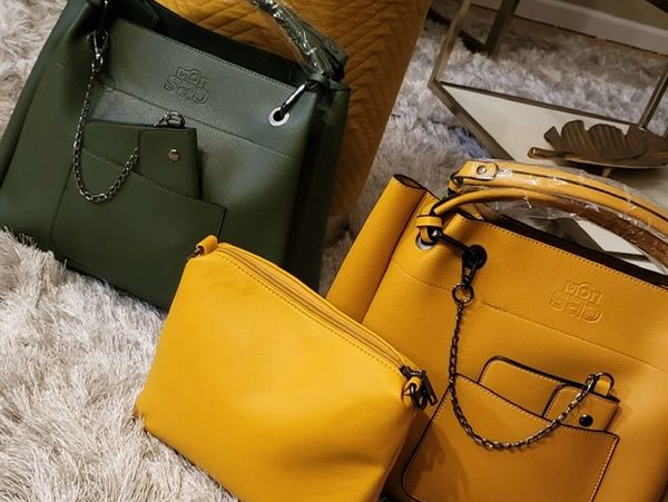 Two stylish handbags and a small pouch on a soft carpet.