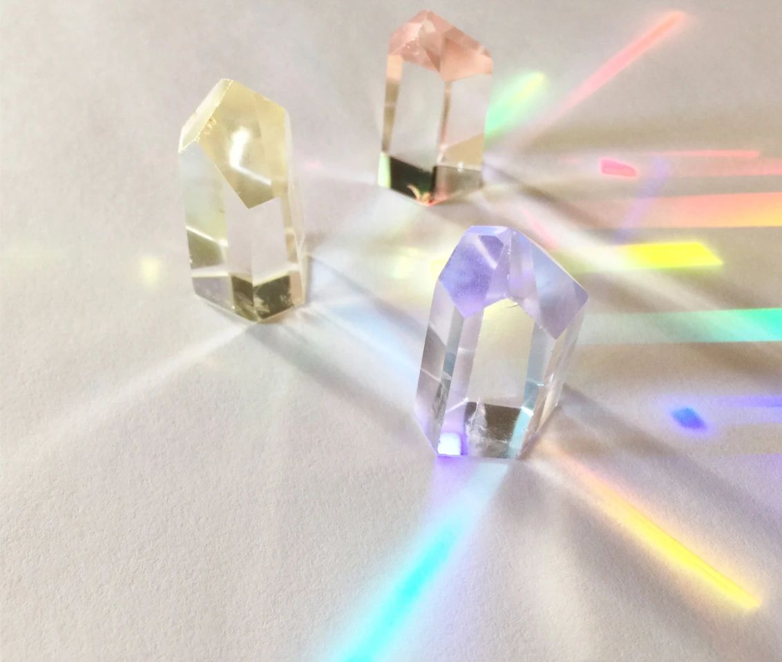 Three colorful crystal prisms casting rainbow light on a white surface.