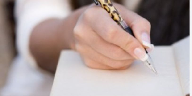 Close-up of a hand writing in a notebook with a leopard-print pen.