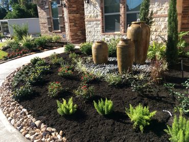 A landscaped garden bed with decorative pots and fresh plants beside a stone house.