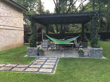 Backyard patio with a hammock under a pergola surrounded by greenery.