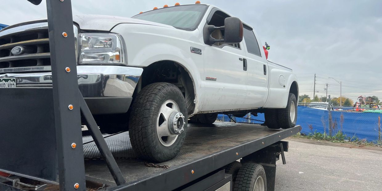 White Ford F-350 truck on a flatbed tow truck under a cloudy sky.