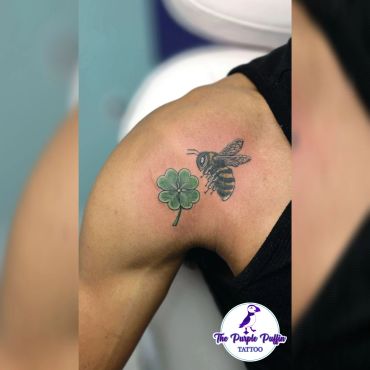 Tattoo of a bee and four-leaf clover on shoulder.