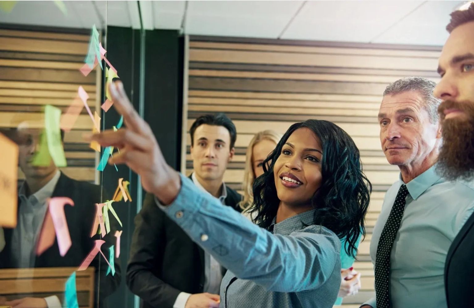 A diverse team collaborates using sticky notes on a glass wall during a brainstorming session.