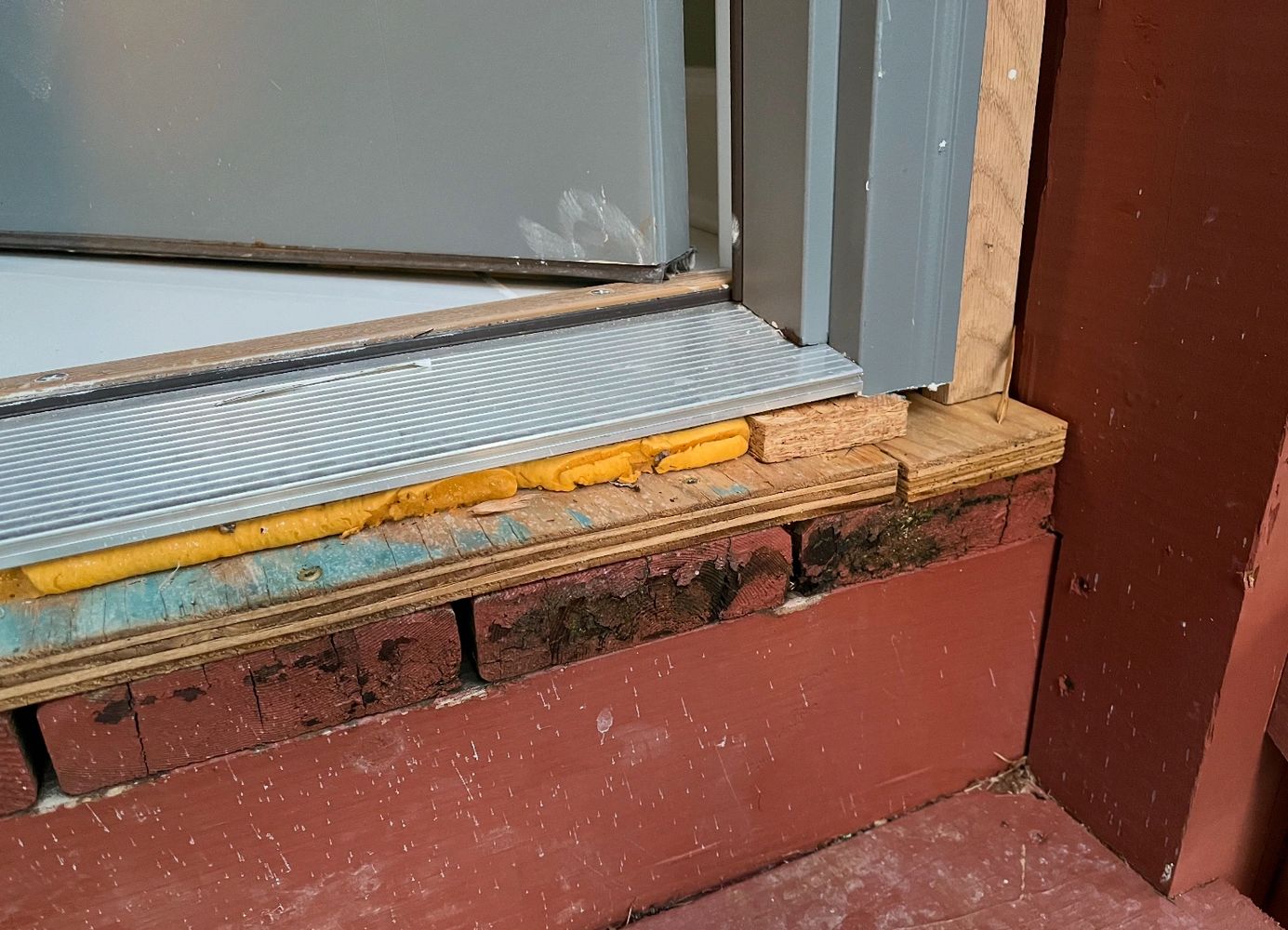 Close-up of a door threshold with visible insulation foam and aged bricks.