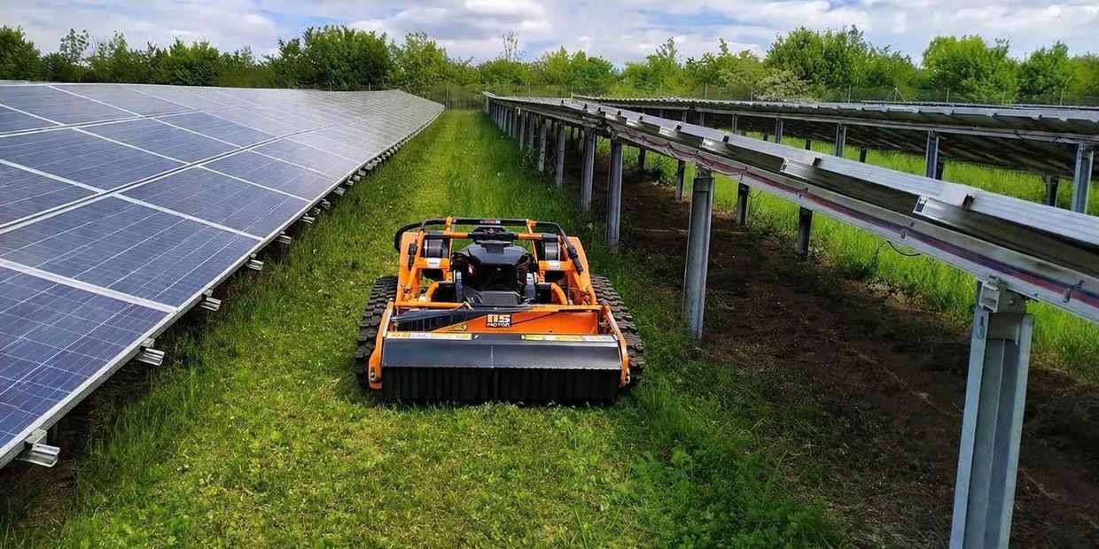 Orange robotic mower cutting grass between solar panel rows.