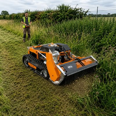 Remote-controlled orange robotic mower cutting tall grass in a field.