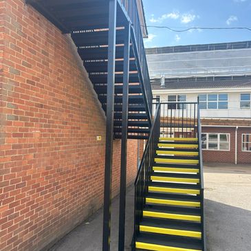 Black metal staircase with yellow steps outside a brick building.