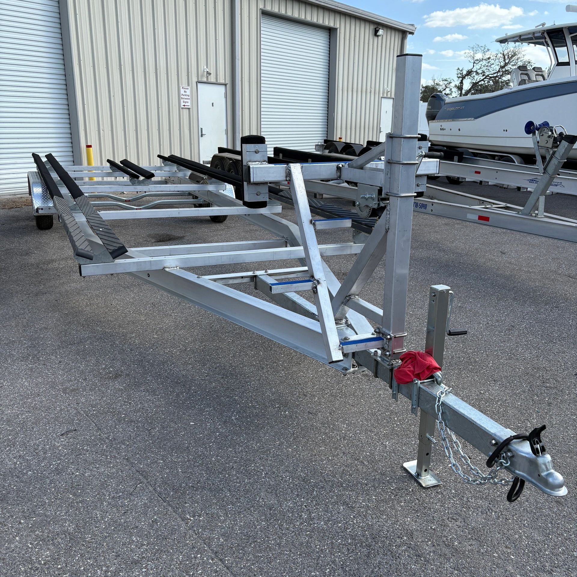 Aluminum boat trailer parked outside a warehouse with a boat in the background.