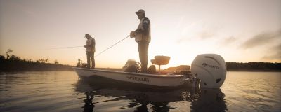 Two men fishing on a boat at sunrise or sunset.