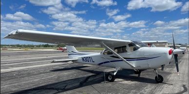 A white Cessna 172 (N30TL) with blue stripes parked on an asphalt ramp.
