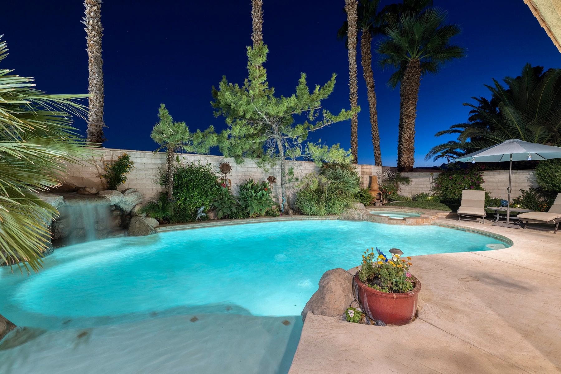 Lighted backyard pool at night showing pool deck propety privacy wall spa plants palm trees