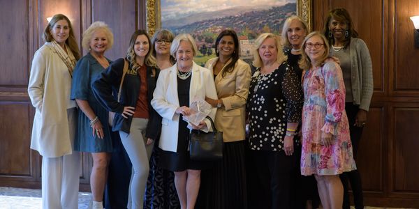 A group of ten women posing indoors in front of a painting.