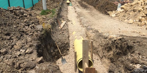 Excavación para instalación de tubería amarilla en suelo con grava.