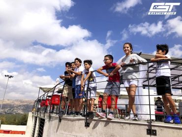 Group of kids standing by railing outdoors on a sunny day.