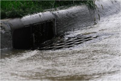 Photo of rain water running down a street storm water drain