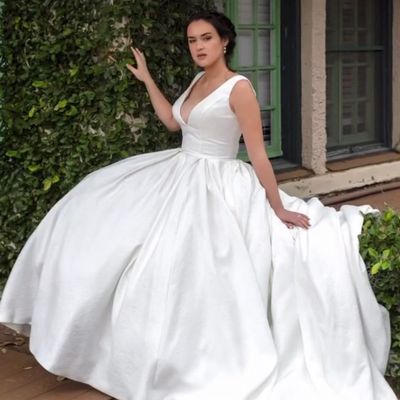 Woman in an elegant white gown posing outdoors near greenery.