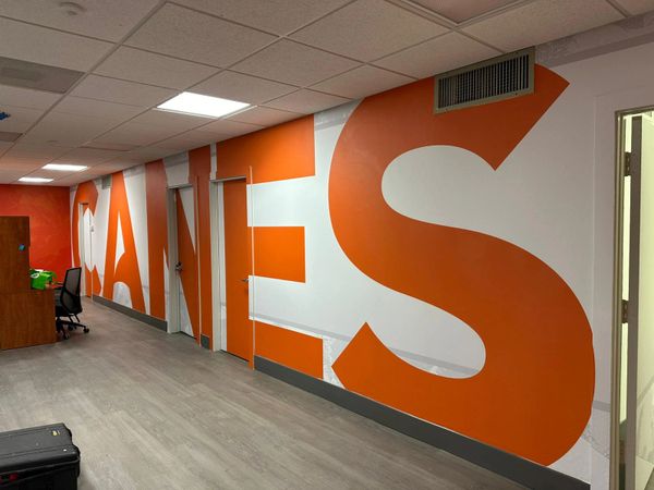 Office hallway with large orange letters spelling 'CANES' on the wall.