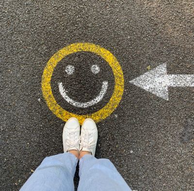 Feet in white shoes near a yellow smiley face and white arrow on asphalt.