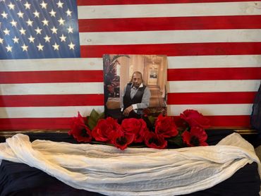 Memorial altar with American flag, photo, red flowers, and white cloth.