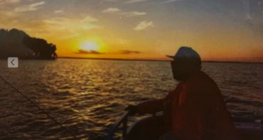 Person fishing on a boat at sunset over calm waters.